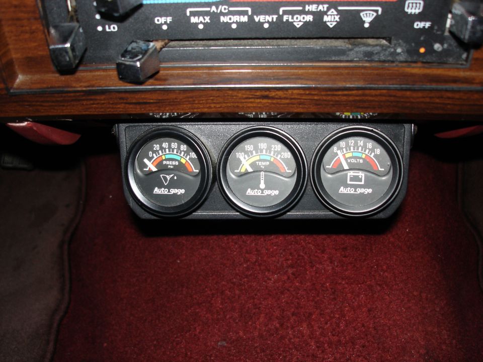 Three Auto Gage brand gauges mounted under a dashboard: oil pressure, engine temperature, and voltage.