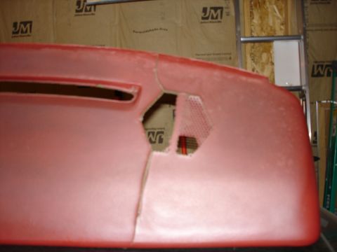 1987 Ford LTD Crown Victoria - A close-up, slightly angled view of a red car part, possibly a bumper or dashboard, with a large cut-out section revealing a mesh vent behi…