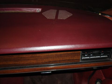 1987 Ford LTD Crown Victoria - A close-up view of a car's dashboard shows a dark red vinyl surface with a wood-grain trim piece below it. A black air vent is visible on t…