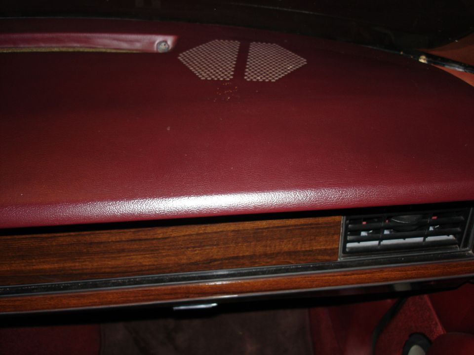 Car dashboard with red vinyl and wood trim, showing an air vent.