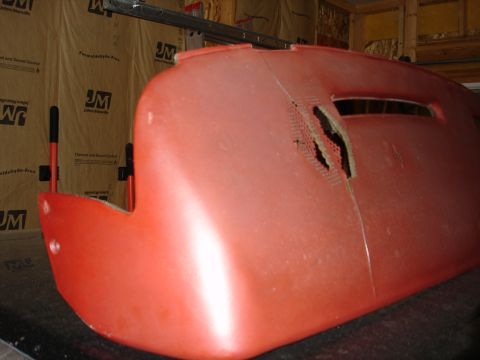 1987 Ford LTD Crown Victoria - A damaged red plastic car dashboard is shown in a workshop setting. The dashboard has a large crack and a section with a perforated pattern…