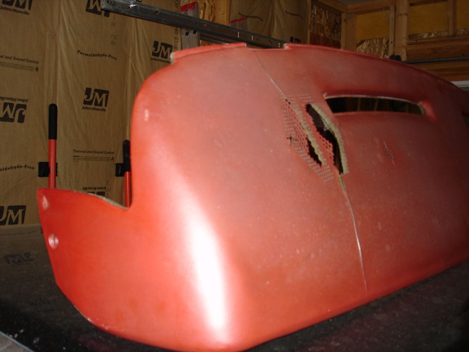 Damaged red plastic car dashboard with a crack and torn perforated section.