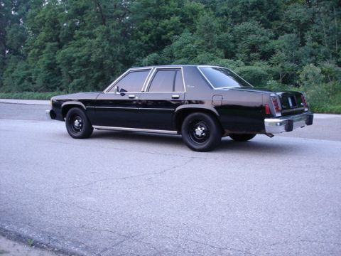 1987 Ford LTD Crown Victoria - A black four-door sedan photographed from the rear three-quarter angle on paved ground, with black steel wheels and a chrome rear bumper, p…