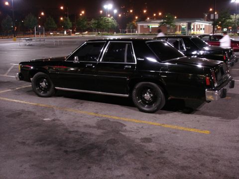 1987 Ford LTD Crown Victoria - A black Ford LTD Crown Victoria four-door sedan shown from the driver's side rear 3/4 angle in a parking lot at night, fitted with black st…