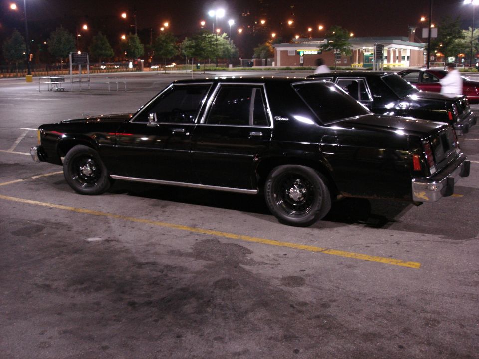 Black Ford Crown Victoria sedan, side/rear view, black steel wheels, night parking lot