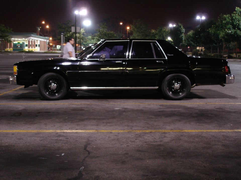 Glossy black Ford sedan side profile at night on black steel wheels with dog-dish caps