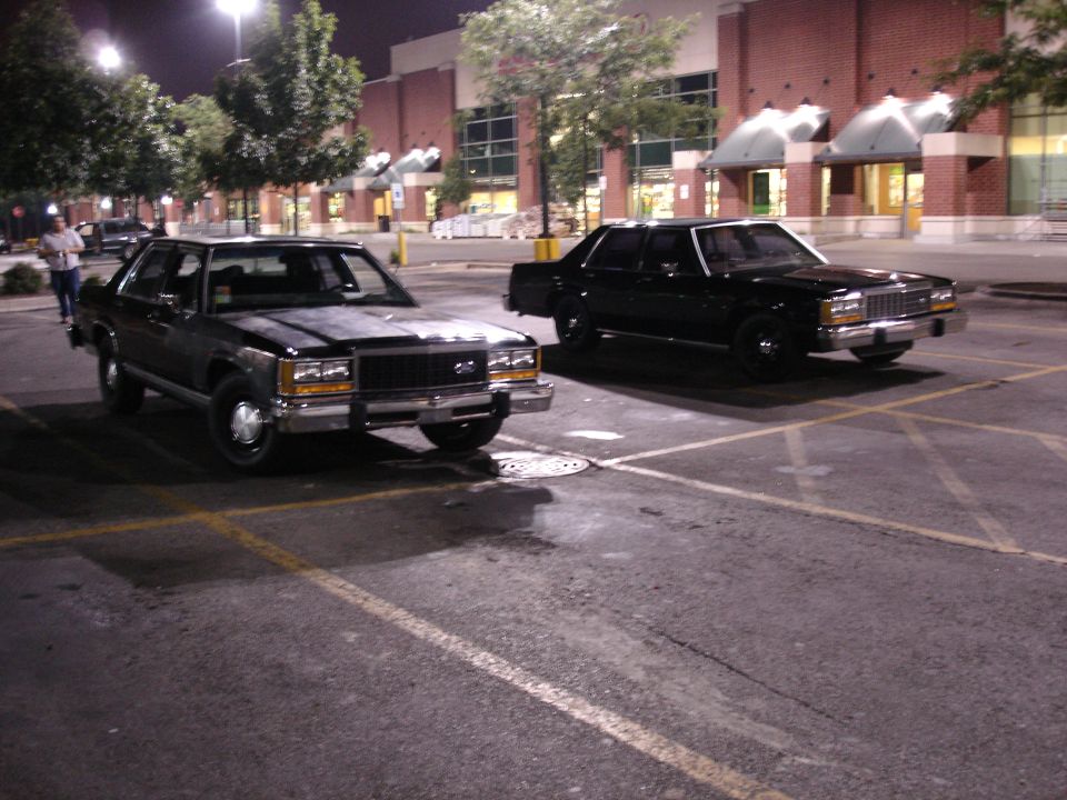 Two black Ford full-size sedans parked at night in a lot, front three-quarter view