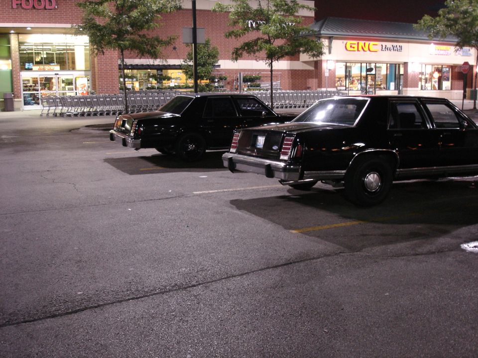 Two black Ford sedans parked rear three-quarter at night outside a grocery store