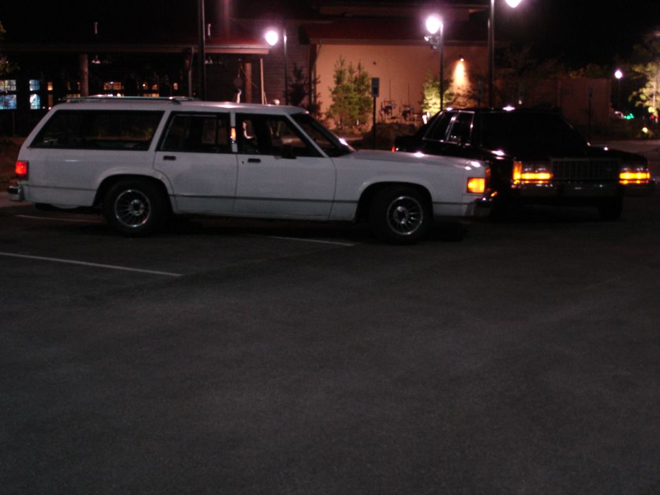 White Ford Crown Victoria station wagon parked next to a black Ford LTD sedan at night.