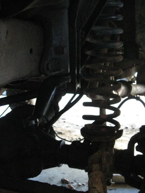 1978 Ford Bronco - Underbody photograph of a coil spring and control arm suspension, not a technical document.