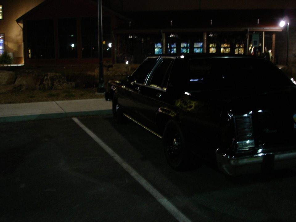 Black sedan parked at night, rear passenger side view.