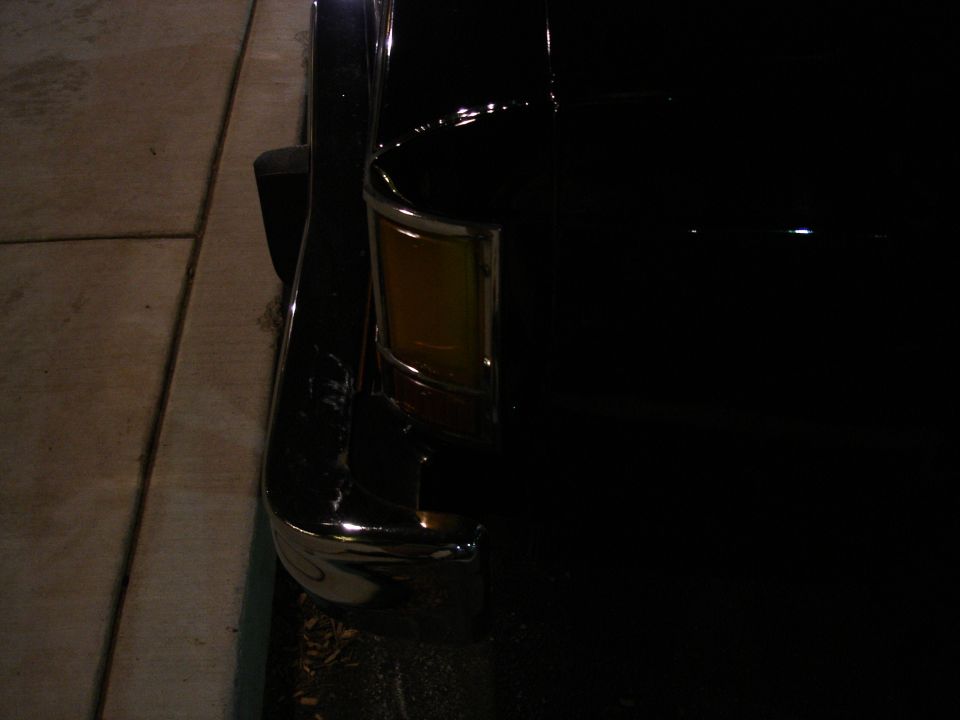 Night close-up of a black car's amber corner turn signal lens and chrome bumper end