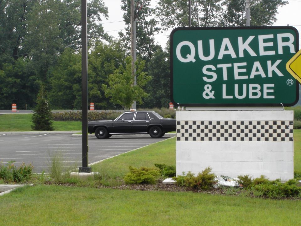 Black four-door Ford sedan in profile beside a Quaker Steak & Lube sign