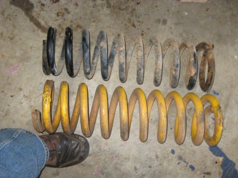 1978 Ford Bronco - Photograph comparing a stock coil spring and a yellow aftermarket coil spring on a floor, not a technical document.