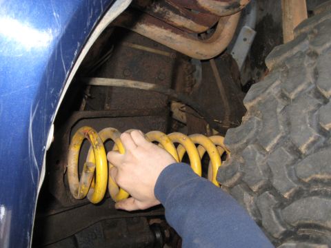 1978 Ford Bronco - Photograph of a yellow coil spring being installed in a vehicle suspension, not a technical document.