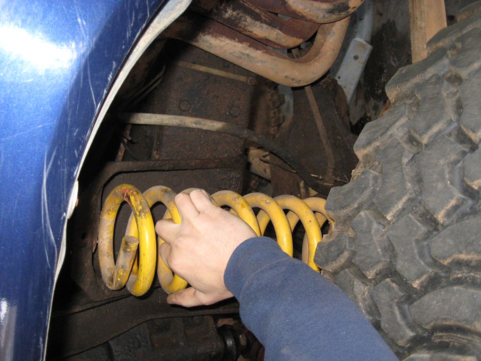 Hand holding a yellow coil spring fitted into a vehicle wheel well
