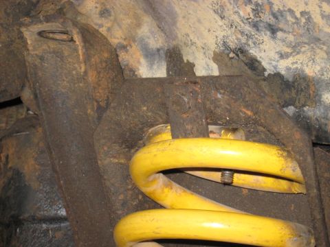 1978 Ford Bronco - Underbody photograph of a yellow coil spring seated on its suspension mount, not a technical document.