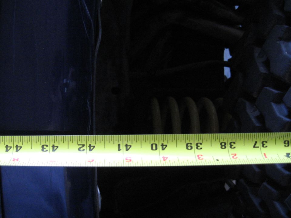 Tape measure across a dark vehicle body panel and coil spring suspension