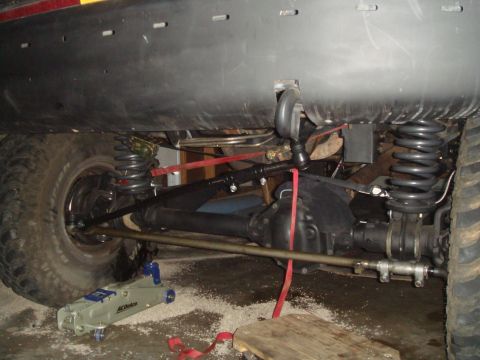 1992 Ford Bronco - The underside of a vehicle is shown, focusing on the front suspension and steering components, including a large tire, coil spring, and dif…