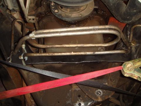 1992 Ford Bronco - The underside of a vehicle showing transmission cooler lines secured with zip ties. A red ratchet strap is also visible, holding components…
