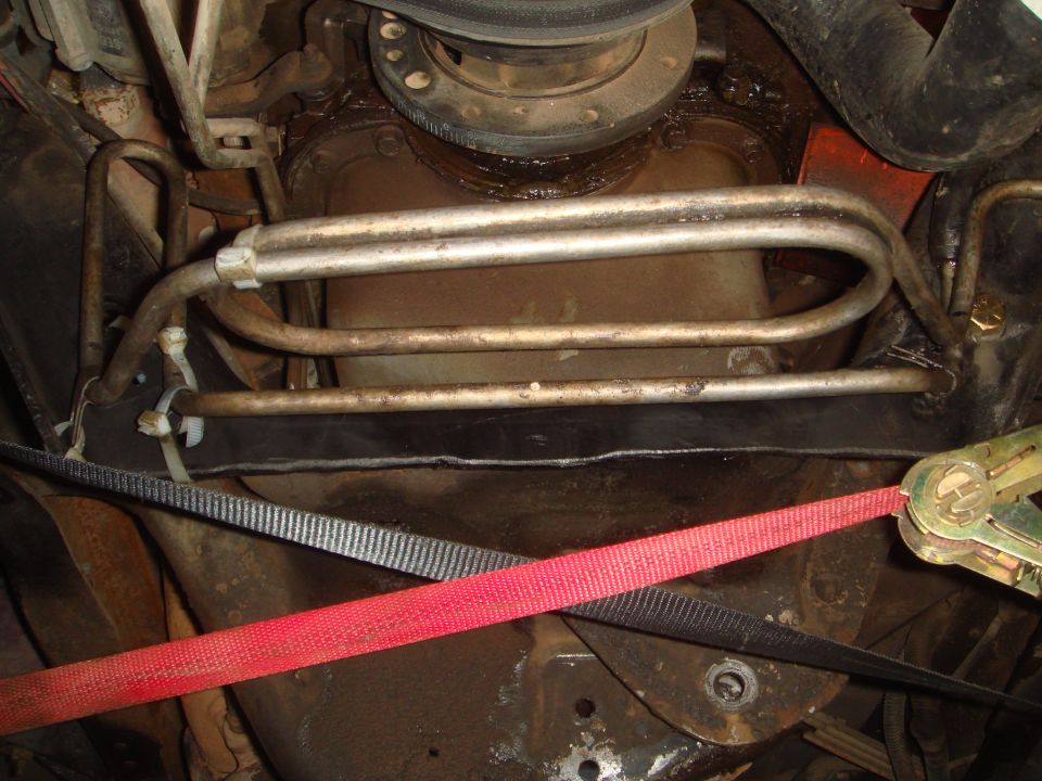 Underside of vehicle with transmission cooler lines and red ratchet strap.