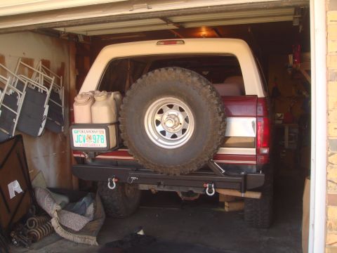 1992 Ford Bronco - The rear of a red and white Ford Bronco is parked in a garage, featuring a spare tire mounted on the back, two gas cans, and an Oklahoma li…