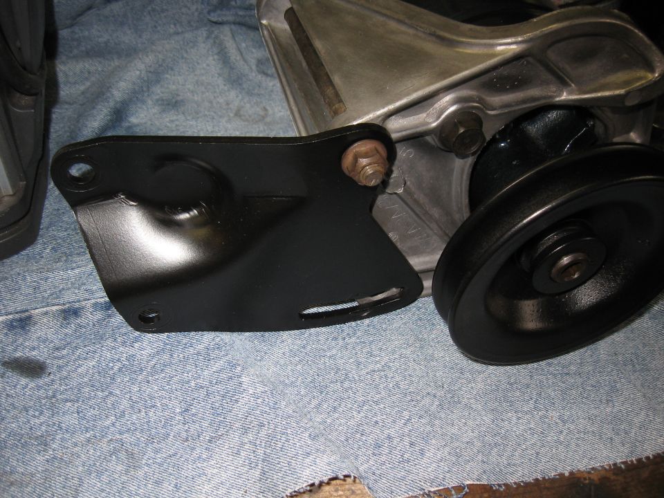Black metal bracket attached to silver component with pulley on denim fabric.