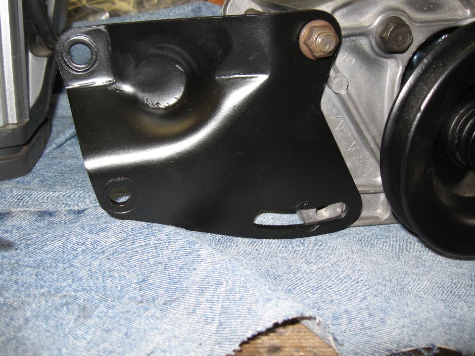 Black metal bracket bolted to silver engine block with pulley.