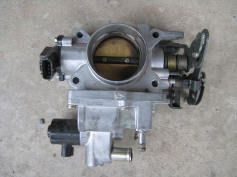 1993 Ford Probe - Throttle body assembly with electrical connector and springs, resting on a concrete surface.
