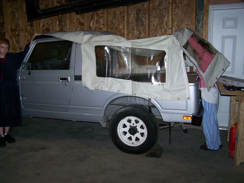 Silver mini 4x4 SUV with tan soft top being fitted in a garage