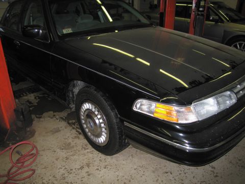 1991 Ford LTD Crown Victoria - Photograph of a black Ford Crown Victoria front fender and headlight in a service bay, not a technical document.