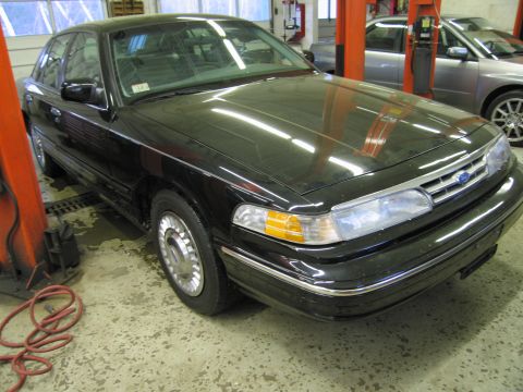 1991 Ford LTD Crown Victoria - Photograph of a black Ford Crown Victoria front three-quarter view in a shop, not a technical document.