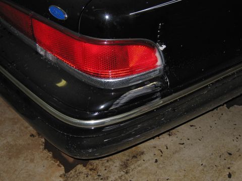 1991 Ford LTD Crown Victoria - Close-up photograph of a black Ford sedan taillight and damaged rear bumper, not a technical document.