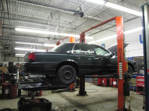 1991 Ford LTD Crown Victoria - Photograph of a dark Ford Crown Victoria raised on a two-post lift in a service shop, not a technical document.