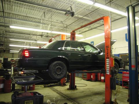 1991 Ford LTD Crown Victoria - Photograph of a dark Ford Crown Victoria rear three-quarter view raised on a shop lift, not a technical document.