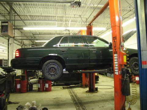 1991 Ford LTD Crown Victoria - Photograph of a dark Ford Crown Victoria side view raised on a two-post shop lift, not a technical document.