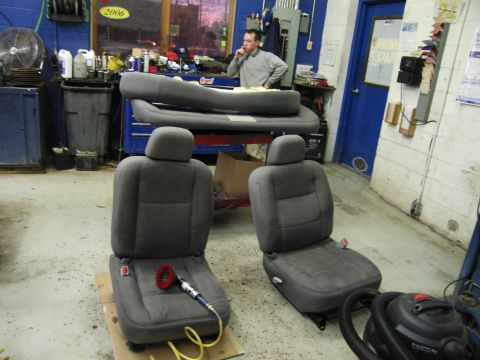 1991 Ford LTD Crown Victoria - Photograph of a pair of gray cloth vehicle seats removed and placed on a shop floor, not a technical document.