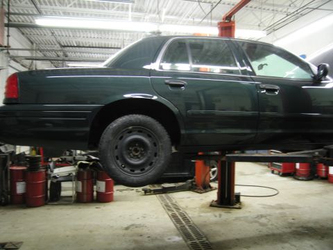 1991 Ford LTD Crown Victoria - Photograph of a dark green sedan lifted on a hoist in a service garage, not a technical document.