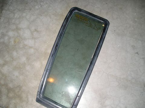 1986 Toyota Hilux - A rectangular automotive glass panel with a black rubber seal is shown lying on a concrete surface. Text and a logo are visible on the glas…