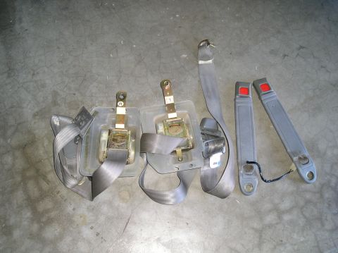 1986 Toyota Hilux - Two gray seatbelt assemblies, each with a retractor mechanism and a metal buckle receiver, are laid out on a concrete surface. To the right…
