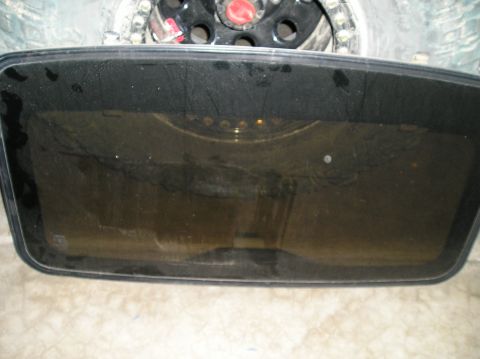 1986 Toyota Hilux - A close-up view of a tinted sunroof with visible water droplets and smudges. In the background, a portion of a tire and wheel assembly is v…
