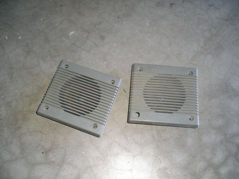 1986 Toyota Hilux - Two gray square speaker grilles with horizontal slats are shown lying on a concrete floor. Each grille has four mounting holes at the corne…