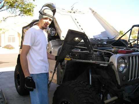 1986 Toyota Hilux - A man wearing a welding helmet and gloves stands next to a silver Jeep Wrangler with its hood open, revealing the engine bay. The Jeep has…