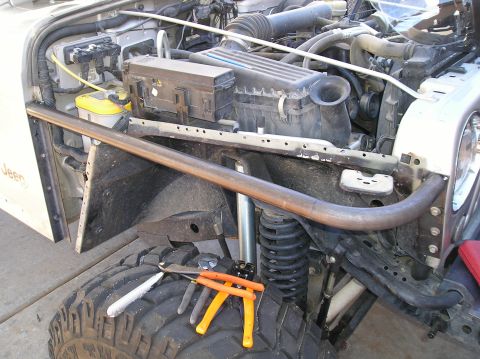 1986 Toyota Hilux - A close-up view of the engine bay and front tire of a Jeep, featuring a custom roll cage tube extending across the front. Tools are laid ou…