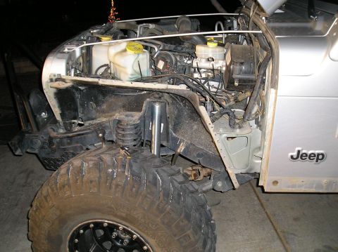 1986 Toyota Hilux - The front driver's side of a silver Jeep Wrangler is shown, with the hood open to reveal the engine bay. The vehicle has large off-road tir…