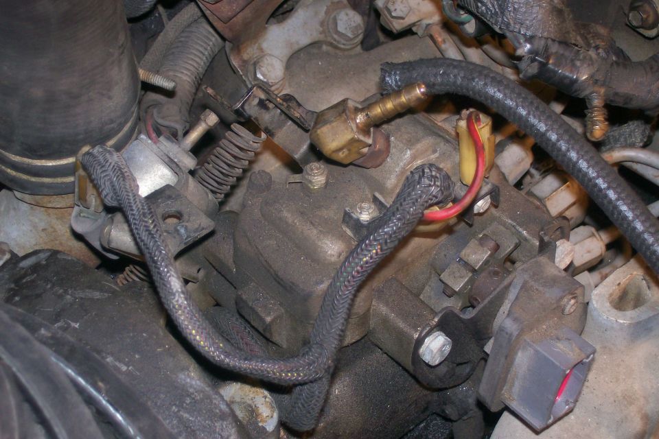Close-up of diesel fuel injection pump with hoses and wiring on a dirty engine.