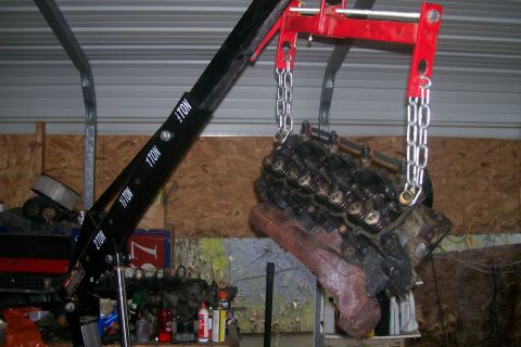 1992 Ford C-350 (Centurion Conversions) - An engine is suspended by chains from an engine hoist in a garage setting.