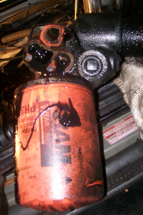 1992 Ford C-350 (Centurion Conversions) - Close-up of an engine part and an oil filter, both heavily coated in oil.