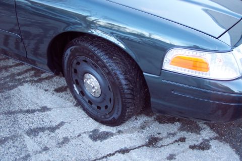 2001 Ford Crown Victoria - The front passenger side of a dark-colored Ford Crown Victoria is visible, with a focus on the wheel and headlight assembly.