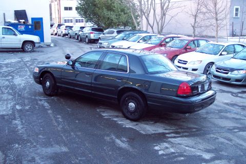 2001 Ford Crown Victoria - A dark 2001 Ford Crown Victoria police car is parked in a lot with other vehicles.